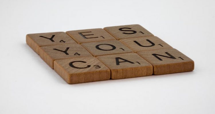 Wooden Scrabble tiles spelling 'Yes You Can' on a white background.